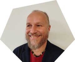 Fachlehrkraft Herr Christian Schöning lächelnd mit schulterlangen, grau-blonden zusammengebundenen Haaren und Vollbart